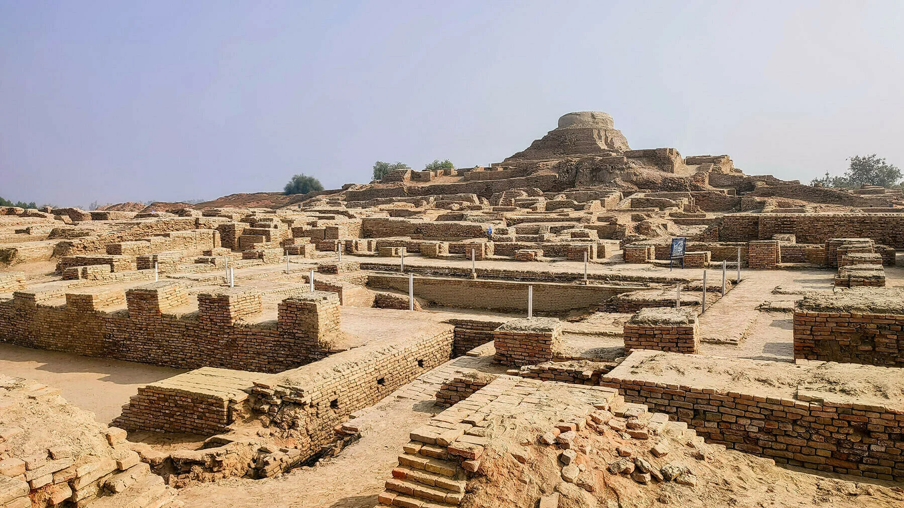 The remnants of an ancient Mohenjo-Daro Pakistani city, showcasing crumbling structures and historical architecture amidst lush greenery.